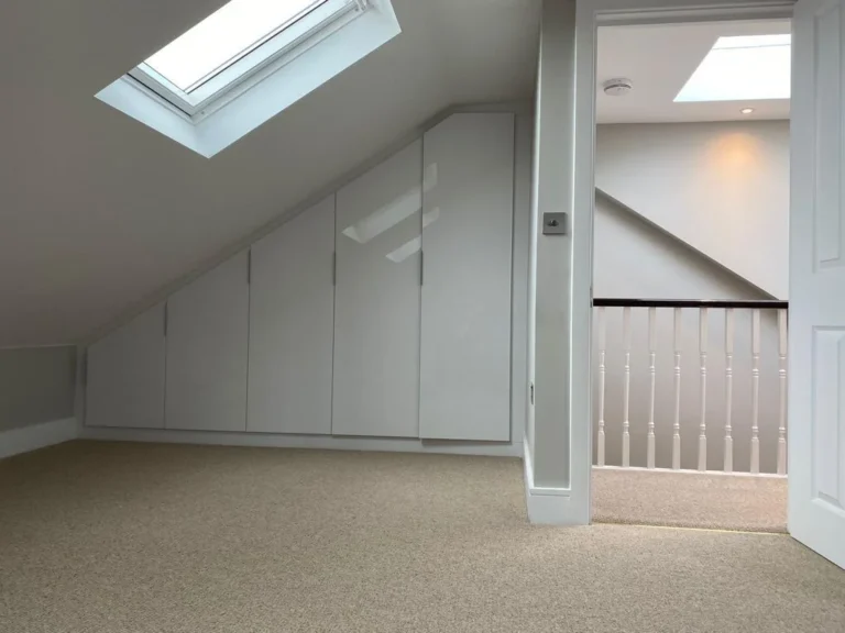 A bright, carpeted loft conversion with built-in storage cabinets and a skylight. Loft Conversions, House Extensions, Roofing, Bespoke Loft Conversions, House Renovations