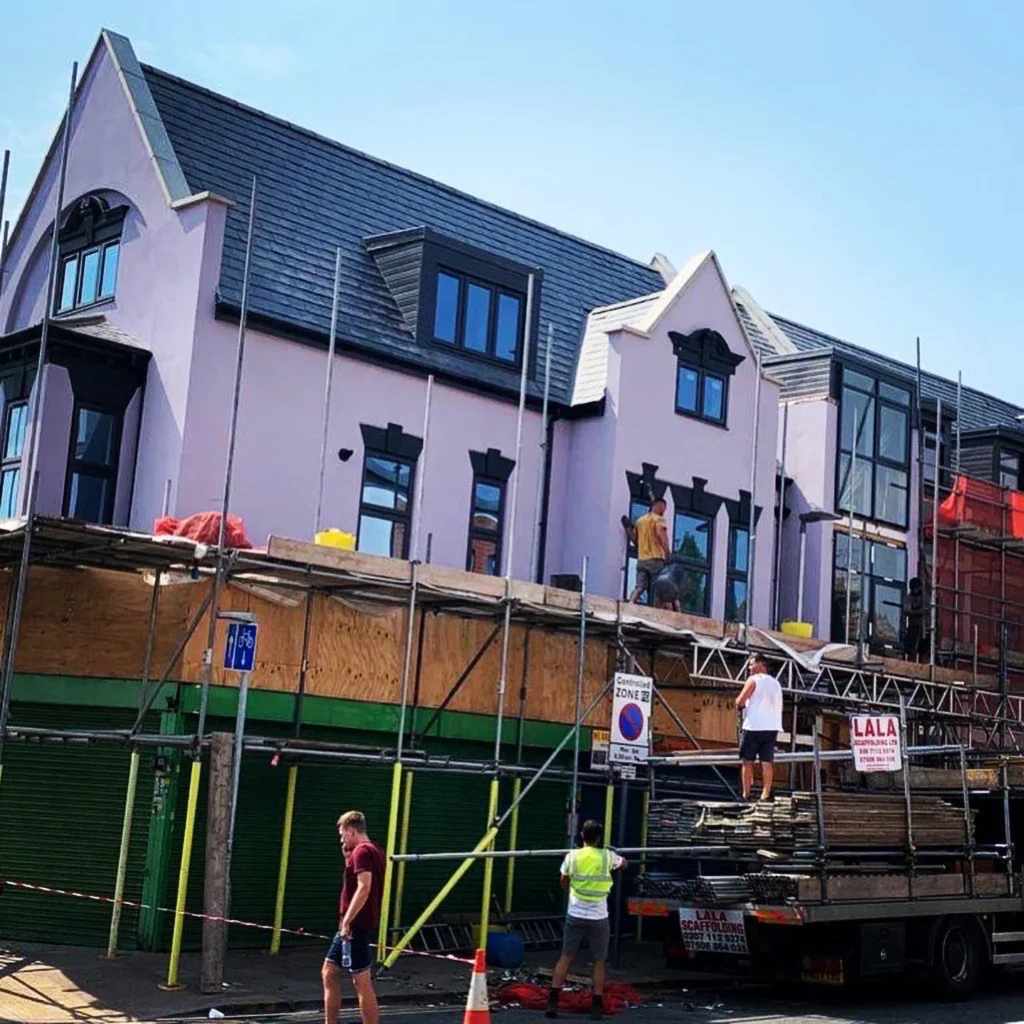Construction workers are active on scaffolding about a partially completed building with distinctive gable roofs. Loft Conversions, House Extensions, Roofing, Bespoke Loft Conversions, House Renovations