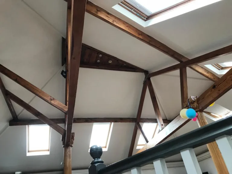 An attic room with exposed wooden beams and skylights featuring roofing details. Loft Conversions, House Extensions, Roofing, Bespoke Loft Conversions, House Renovations