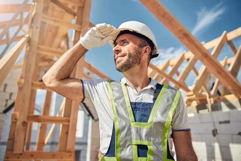 Construction worker in reflective vest and helmet looking into the distance at a building site, observing our process. Loft Conversions, House Extensions, Roofing, Bespoke Loft Conversions, House Renovations